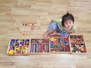 High angle view of girl with colorful craft products sitting on hardwood floor at home
