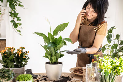 Female gardener talking by phone working at workshop transplantation houseplants