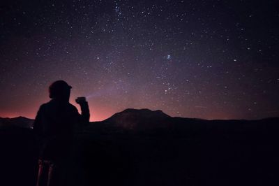 Low angle view of man standing on hill against sky at night