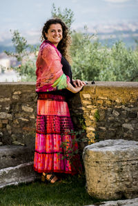 Full length portrait of happy woman standing by retaining wall