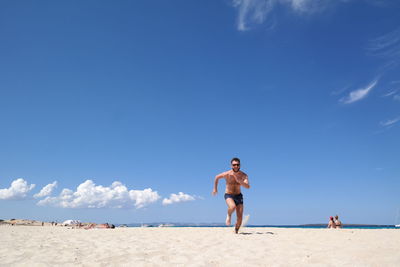 Full length of men sitting on beach against sky