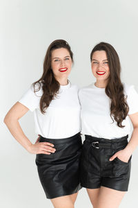 Two beautiful women twin sisters posing white background