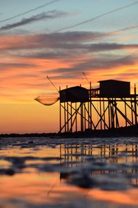 Silhouette fishing net on sea against sky during sunset