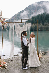 A loving married couple the bride and groom in suits celebrate wedding near the mountains and water