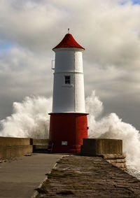 Low angle view of lighthouse by building against sky with crashing waves