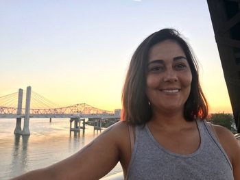 Smiling young woman against suspension bridge during sunset