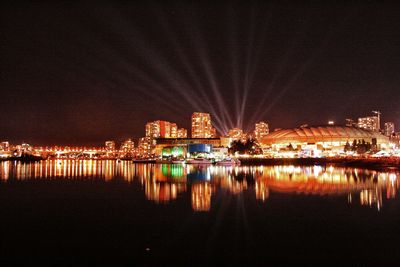 Illuminated buildings by river against sky at night