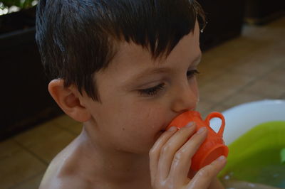 Close-up of cute boy holding toy cup while sitting in bathtub at home