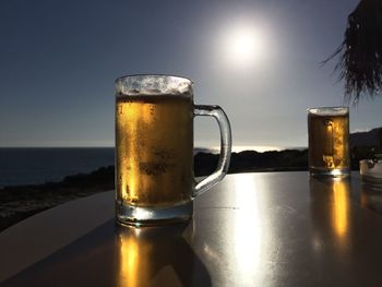 Close-up of beer glass on table against sea during sunset