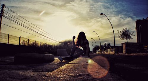 Woman sitting on sidewalk against sky