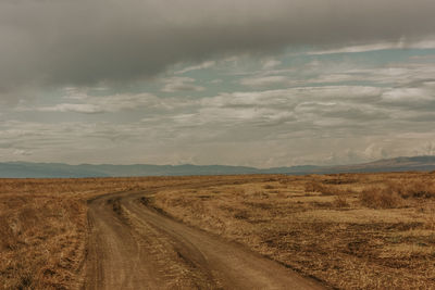 Dirt road amidst field against sky