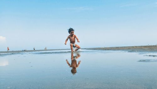 Shirtless boy running at beach against sky