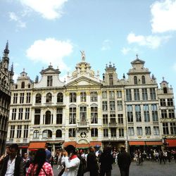 People walking in city against cloudy sky