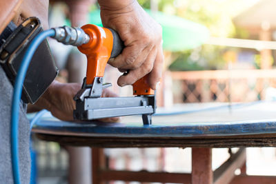 Midsection of worker using power tool on table in workshop