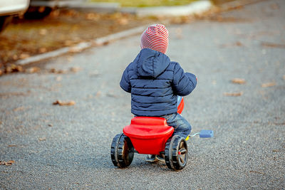 Rear view of boy riding tricycle on street during winter