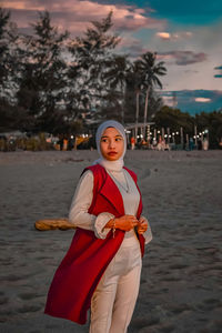 Portrait of beautiful young woman standing on land against trees