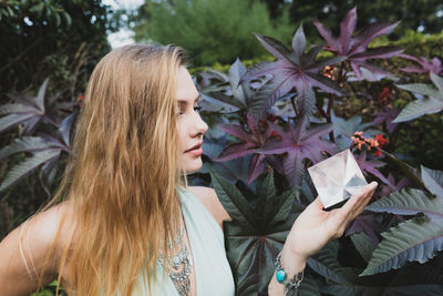 Young woman looking at prism while standing against plant