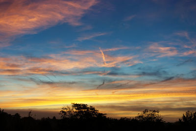 Low angle view of silhouette trees against dramatic sky