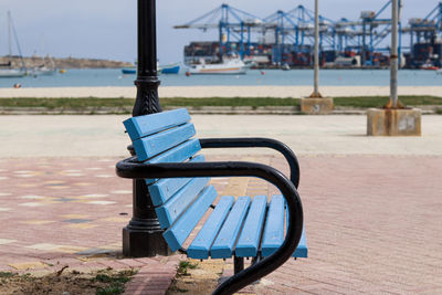 Empty bench on pier by sea against blue sky