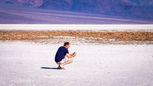 Full length of man crouching on land during sunny day