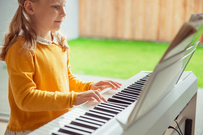Midsection of girl playing piano while sitting at home
