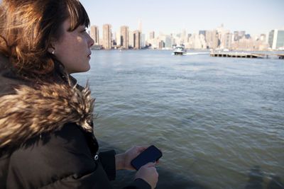 Side view of woman looking away while traveling in ferry against buildings