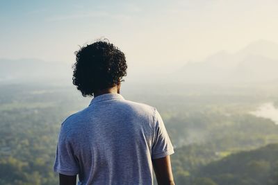 Rear view of mid adult man looking at landscape while standing on mountain against sky