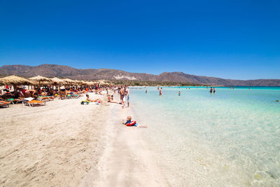 People at beach against clear blue sky