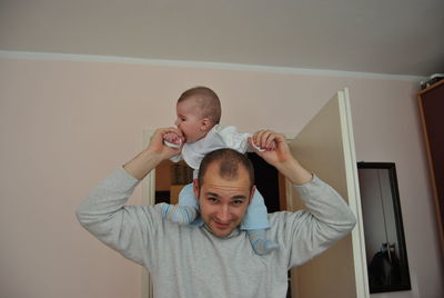 Portrait of father carrying son on shoulders at home