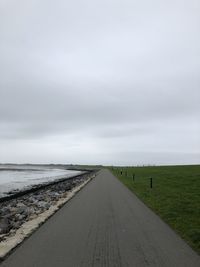 Empty road near sea dike amidst field against sky 