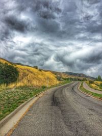 Road passing through field against cloudy sky