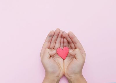 Close-up of hand holding heart shape over white background