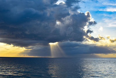 Sunlight streaming through clouds in sea during sunset