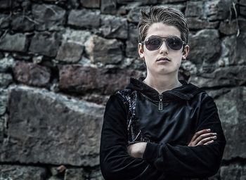 Portrait of young man wearing sunglasses standing against brick wall