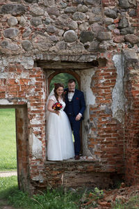 Full length of newlywed couple standing by abandoned built structure