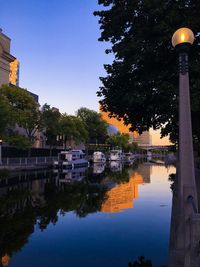 Illuminated buildings by river against sky at dusk