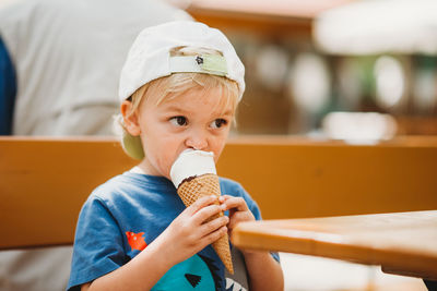 Blonde toddler eating ice cream cone sitting on bear garden bench