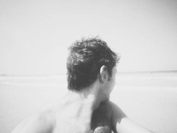 Rear view of shirtless man at beach against sky