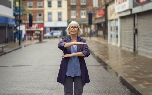 Portrait of woman gesturing while standing on footpath against buildings