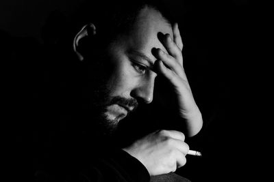 Thoughtful man smoking cigarette against black background