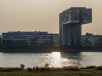 People on beach by buildings against sky during sunset