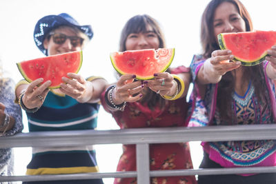 High angle view of friends holding watermelon slices while standing against sky