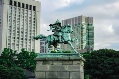 Low angle view of statue against modern buildings in city