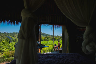 Woman using laptop against plants seen through bed