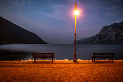 Illuminated lamp by lake against sky at night