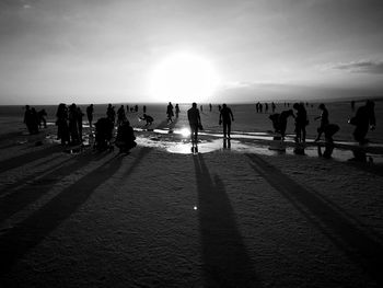 Silhouette people on beach against sky during sunset