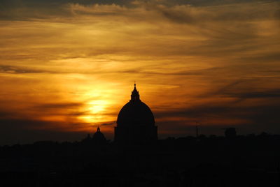 Silhouette temple against building during sunset