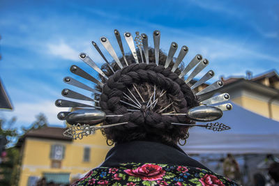 Rear view of woman with decorated spoons and braided hair against sky