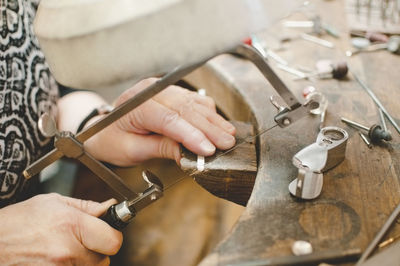 Cropped image of senior woman cutting metal with hand saw in jewelry workshop