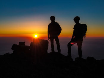 Silhouette people standing on rock by sea against sky during sunset
